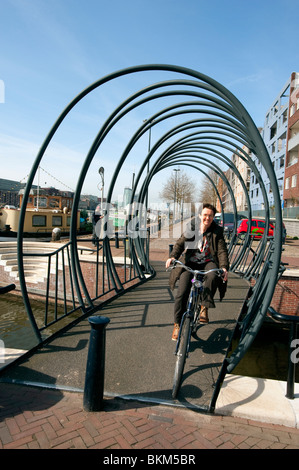 Radfahrer kreuzen moderne stählerne Fußgängerbrücke über Kanal im Neubaugebiet der Insel Java in Amsterdam Niederlande Stockfoto