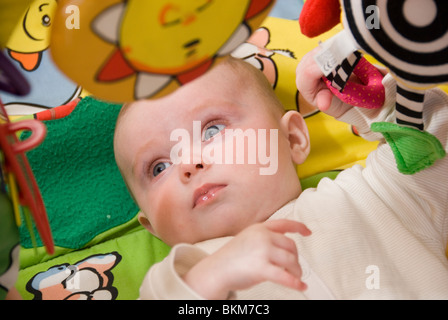 Babymädchen entwickeln Motorsteuerung spielt beim Fang der hängenden Spielzeuge der bunten Babygym Stockfoto