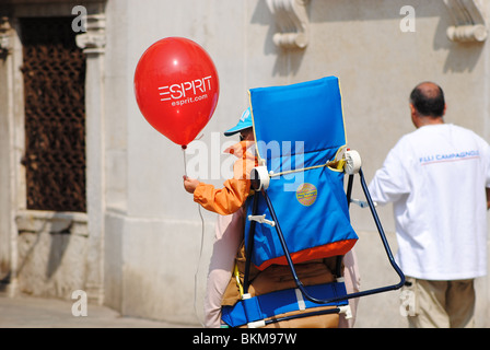 Ein Baby trägt einen Ballon in einem Stuhl auf seine Mutter zurück, Venedig, Italien Stockfoto