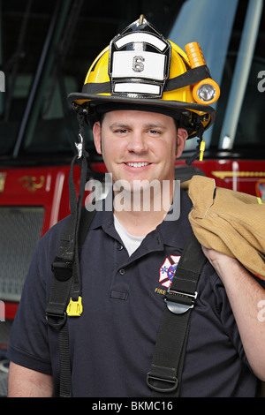 gut aussehend Feuerwehrmann in seinen zwanziger Jahren trägt Helm und hält einheitlichen Stand vor Feuerwehrauto Nahaufnahme Stockfoto