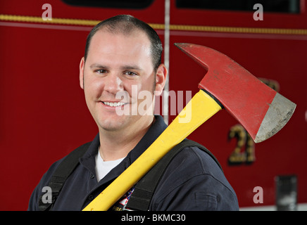 Erwachsenen Feuerwehrmann lächelnd und halten Feuer Axt vor Feuerwehrauto closeup Stockfoto