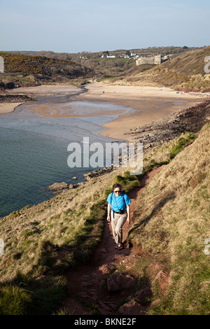 Weiblich, zu Fuß auf dem Pembrokeshire Coast Path bei Manorbier mit Strand und Burg im Hintergrund Wales UK Stockfoto