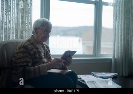 Alte Frau sitzt im Stuhl von Fenster und kleines Fotoalbum blättert. Stockfoto