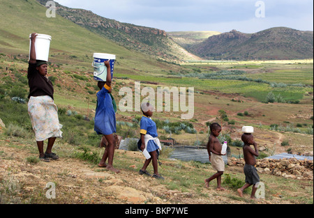 Lesotho: Familie Wasser aus einem Brunnen im Eimer auf dem Kopf tragen Stockfoto