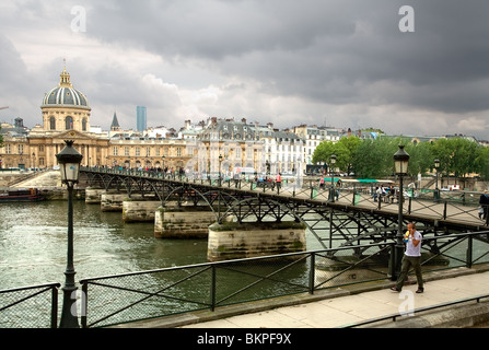Fußgänger zu Fuß auf die Brücke Pont des Arts und Ansicht des Institut de France in Paris, Frankreich unter Gewitterhimmel. Stockfoto