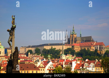 Tschechische Republik, Prag; Auf der Karlsbrücke eine Skulptur des Gekreuzigten, mit Pragerburg hinter. Stockfoto