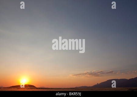 Afrika, Namibia, Damaraland, Brandberg Mountain. Die Sonne geht über den Ausläufern Stockfoto
