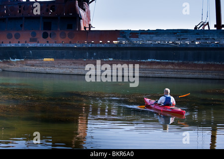 Ein einsamer Kajakfahrer, Reisen durch stehende Gewässer mit einem Schiffbruch hinter, auf See Ontario, Kanada. Stockfoto