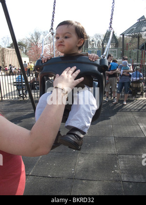 Einjähriger Junge auf der Schaukel mit Mama im Prospect Park, Brooklyn, NY Stockfoto