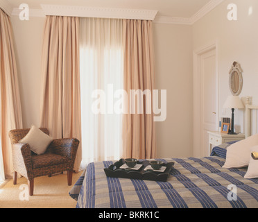 Blaue aufgegebenes Bettdecke im Bett im modernen Schlafzimmer mit Beige Vorhänge und braune Sessel Stockfoto