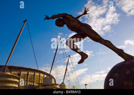 Die Läufer-Skulptur am Sportcity, Manchester: City of Manchester Stadium hinter Stockfoto