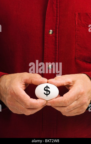 Mann hält weißes Ei mit einem Dollarzeichen ($) geschrieben steht, als Symbol für die Zerbrechlichkeit von Geldangelegenheiten; die sprichwörtliche "Notgroschen". Stockfoto