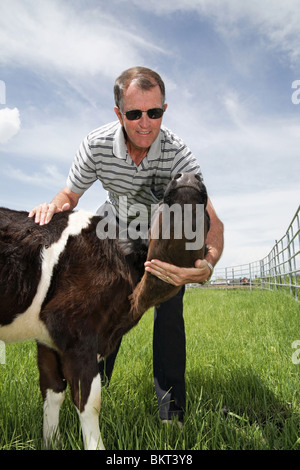 Viehzüchter in Freizeitkleidung mit schwarzen und weißen Kalb in einem Land spielen Stockfoto