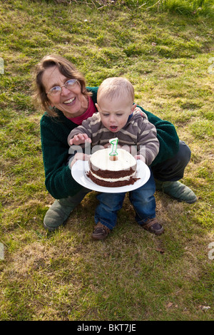 Einjährigen jungen draußen mit seiner Geburtstagstorte und Großmutter, Hampshire, England, Vereinigtes Königreich. Stockfoto