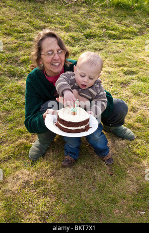 Einjährigen jungen draußen mit seiner Geburtstagstorte und Großmutter, Hampshire, England, Vereinigtes Königreich. Stockfoto