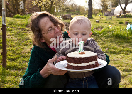 Einjährigen jungen draußen mit seiner Geburtstagstorte und Großmutter, Hampshire, England, Vereinigtes Königreich. Stockfoto