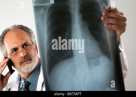 Bild eines Arztes Brillen-und einen weißen Kittel und Blick unverwandt auf eine Röntgenaufnahme beim mit seinem Handy. Stockfoto