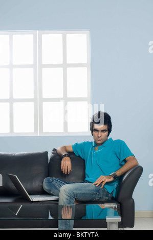 Junger Mann sitzt vor Laptop, Porträt Stockfoto