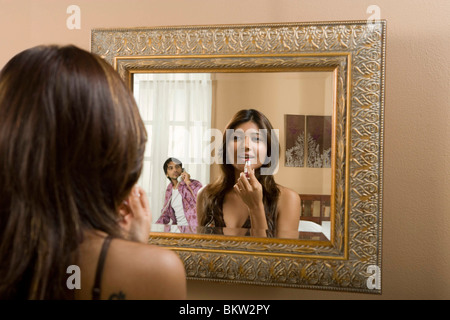 Frau Auftragen von Lippenstift vor Spiegel mit Reflexion der Mann am Telefon Stockfoto