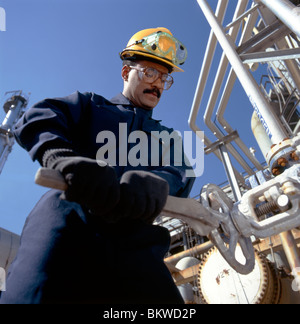 Afrikanische amerikanischer Arbeiter mit einem großen Schraubenschlüssel dreht sich ein Ventil mit einer Ölraffinerie in Delaware, USA Stockfoto