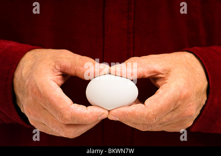 Ein Mann hält ein weißes Ei. Symbolisieren könnte die Zerbrechlichkeit von Geldangelegenheiten und den sprichwörtlichen "Notgroschen". Stockfoto