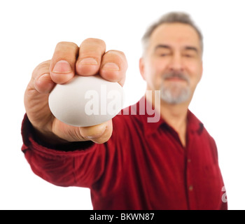Reifer Mann hält ein weißes Ei in der ausgestreckten Hand. Stockfoto