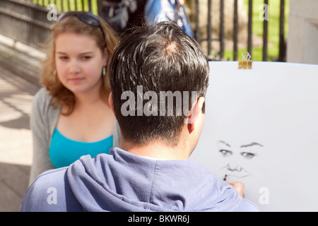 Ein junges Mädchen sitzen für ihr Porträt von einem Straßenkünstler, Leicester Square, London UK Stockfoto