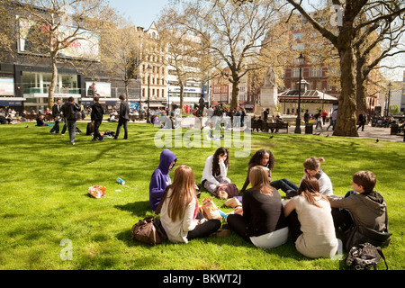 Eine Gruppe von Jugendlichen saß auf dem Gras im Sommer Sonnenschein, Leicester Square, London, Großbritannien Stockfoto