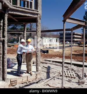 Zwei männliche Führungskräfte Überprüfung Architekturzeichnungen auf einer Baustelle von einem Neubau der Unternehmenszentrale Stockfoto