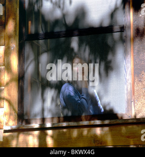 Sonne gefleckten Porträt der jungen Frau angesehen durch geschirmte Fenster von einem Blockhaus im Adirondack Park, Upstate New York, USA Stockfoto