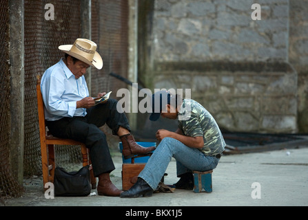 Ein Mann liest das Papier wie ein Schuhputzer seine Stiefel in Cuetzalan del Progreso, Mexiko reinigt Stockfoto