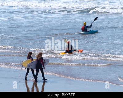 Zwei Surf-Kanuten paddeln, und weibliche Surfer in Richtung Meer, Cornwall Stockfoto