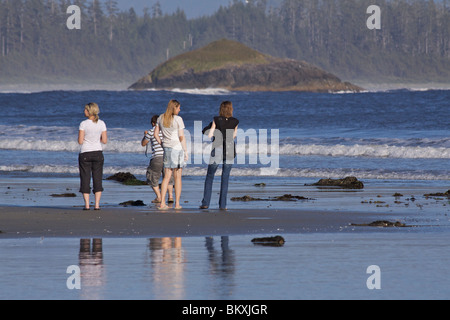 Drei junge Frauen und ein junger Mann auf Chesterman Beach in Cox Bay beobachten die Wellen in in der Nachmittagssonne, in der Nähe von Tofino Stockfoto