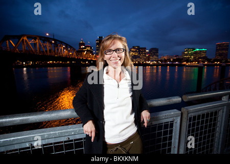 Die Frau stützte sich auf Geländer vor Willamette River mit Citylights in den Nachthimmel. Stockfoto