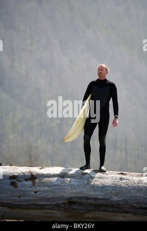 Ein Mann steht auf einen umgestürzten Baum mit seinem Surfbrett auf The Lost Coast, Kalifornien. Stockfoto