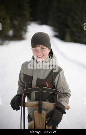 Ein Portrait eines jungen Jungen und seinen Schlitten draußen auf einer verschneiten Straße. Stockfoto