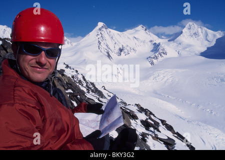Mann hoch auf einem schneebedeckten Gipfel mit einer Karte und einem weiten Blick auf Winter in Alaska. Stockfoto