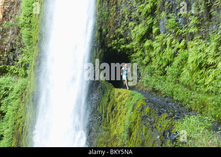 Eine Frau rennt weg gesprengt in einen Hügel hinter einem Wasserfall auf der Pacific Crest Trail, Oregon. Stockfoto