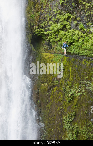 Eine Frau, Wandern entlang gestrahlt in einem Hügel hinter einem Wasserfall auf der Pacific Crest Trail, Oregon Trail. Stockfoto