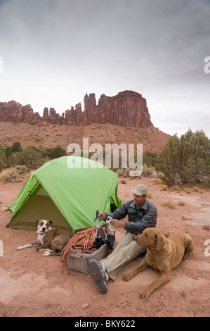 Ein Mann Sortierung Kletterausrüstung auf einem Campingplatz mit seinen zwei Hunden, Indian Creek, Monticello, Utah. Stockfoto