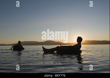 Ein junges Paar entspannen Sie bei einem kühlen Drink und Schwimmen in einem See bei Sonnenuntergang in Schläuche. Stockfoto