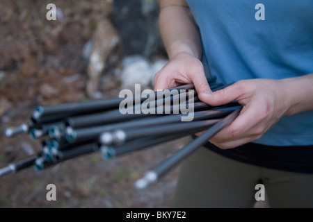 Weibliche Backpacker in ihren frühen dreißiger Jahren untersucht ihr Aluminium Zeltstangen während pitching ihr Zelt. Stockfoto