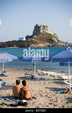 Menschen, die zum Sonnenbaden in Kefalos Beach, Insel Kastri mit Kapelle St. Nikolaus in Hintergrund, Kefalos, Kos, Griechenland Stockfoto