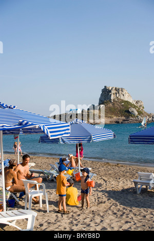 Menschen, die zum Sonnenbaden in Kefalos Beach, Insel Kastri mit Kapelle St. Nikolaus in Hintergrund, Kefalos, Kos, Griechenland Stockfoto