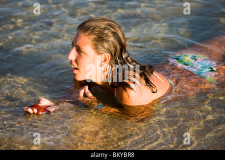 Frau im Flachwasser im Paranga Beach liegen und hielt einen Seestern in der Hand, Mykonos, Griechenland Stockfoto