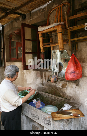 Hongkou Quartal Shanghai, alte Dame, die Reinigung von Gemüse, Backstreet, kommunale Waschbecken, Spiegel, Stuhl aus Bambus Stockfoto