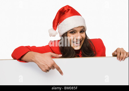 Frau in Santa Kostüm zeigt auf eine weiße Tafel und lächelnd Stockfoto
