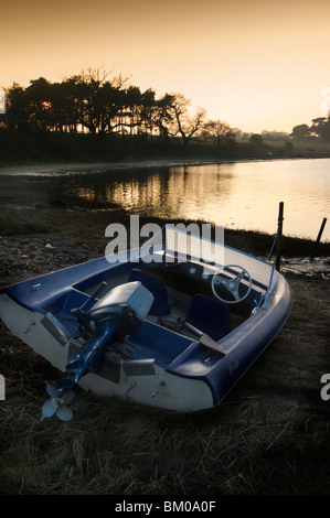 Einem kleinen Motorboot am Ufer eines Flusses mit Abendsonne hinter Bäumen, Suffolk England Stockfoto