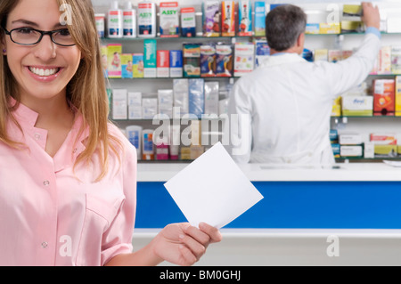 Apothekerin hält ein Rezept und einen männlichen Apotheker im Hintergrund Stockfoto