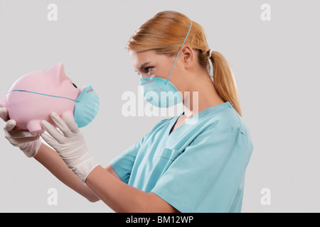 Ärztin eine Schornstein-Maske trägt und hält ein Sparschwein Stockfoto